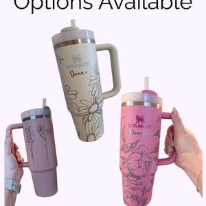 May include: Three Stanley tumblers with handles and straws, featuring custom floral line art engravings and the name Donna. The tumblers are cream, dusty rose, and bright pink. Text at the top reads Custom Order Options Available and The Lilac Nook.