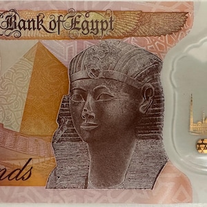 Puede incluir: Un billete de diez libras egipcias con un retrato de un faraón, pirámides y una mezquita. El billete presenta el texto "Central Bank of Egypt" y "Ten Pounds". El billete es principalmente de color marrón, beige y dorado.