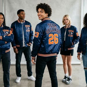 Könnte beinhalten: Eine Gruppe von Personen trägt marineblaue Satin-Bomberjacken mit orangefarbenen und weißen Akzenten. Die Jacken tragen den Text "TEAM CLUB" und Zahlen auf den Ärmeln und dem Rücken. Klassischer Varsity-Stil.