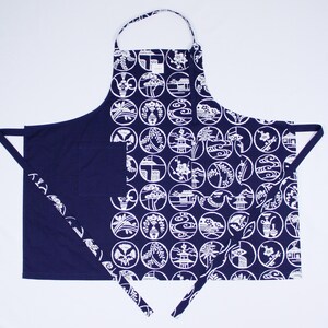 Può includere: Un grembiule blu navy con un motivo bianco di cerchi contenenti disegni di ispirazione giapponese. Il grembiule ha una grande tasca sul davanti e lacci regolabili.