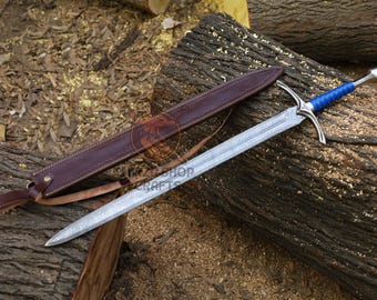 May include: A silver sword with a blue handle and a brown leather sheath rests on a wooden log. The sword has a long, pointed blade and a crossguard. The sheath is closed with a strap.
