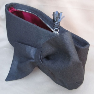 May include: A black canvas clutch bag with a large bow detail and a black tassel zipper pull.
