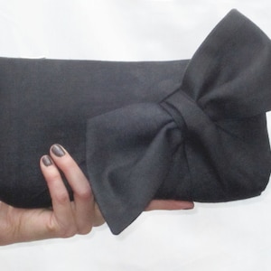 May include: A black fabric clutch with a large bow on the front.