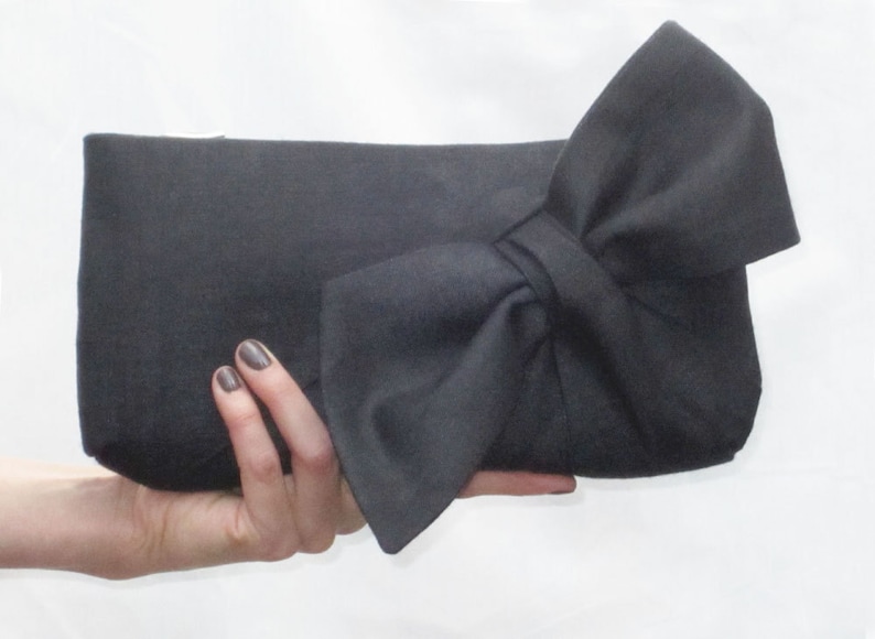 May include: A black fabric clutch with a large bow on the front.
