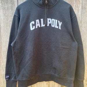 May include: A white ceramic mug with a black handle and the text "But First, Coffee" in a bold, black font. The mug is set against a blurred background, suggesting a cozy setting.