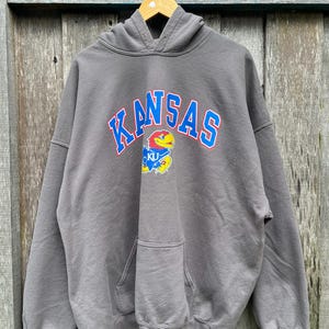May include: Gray hooded sweatshirt with a blue and red "KANSAS" graphic and a yellow and blue mascot.