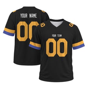 Op de afbeelding: Een zwart shirt met V-hals, voorzien van de tekst YOUR TEAM en het nummer 00 in goud op de voorzijde. De mouwen hebben gouden en paarse strepen. De achterzijde toont de tekst YOUR NAME en het nummer 00 in goud, met bijpassende mouwstrepen.