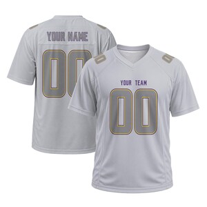 May include: A light gray V-neck sports jersey featuring the text YOUR NAME and the number 00 on the back, and the text YOUR TEAM with the number 00 on the front. The jersey has short sleeves and includes small rectangular accents on the shoulders.