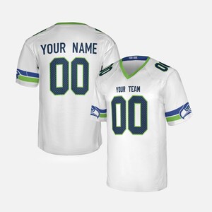 Pode incluir: Camisola de futebol branca com detalhes verdes e azuis. A camisola apresenta o número "00" num padrão azul escuro em forma de grelha, com o texto "YOUR NAME" e "YOUR TEAM" acima dos números. Tem decote em V e mangas curtas.