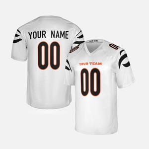 May include: A white sports jersey featuring black tiger stripe patterns on the sleeves. The front displays the text YOUR TEAM and the number 00 in black with orange outlines. The back shows the text YOUR NAME and the number 00 in black.