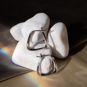 May include: Two silver triangle-shaped hoop earrings on white stones.