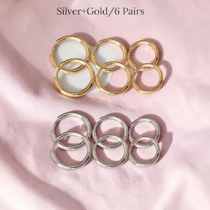 May include: Six pairs of hoop earrings in gold and silver tones are arranged on a pink surface. The earrings are of varying sizes, with three pairs in gold and three pairs in silver. The text "Silver+Gold/6 Pairs" is at the top.