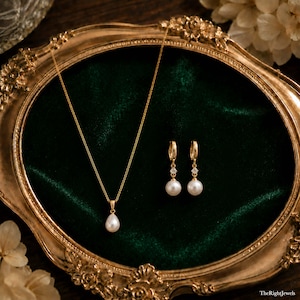May include: A gold necklace featuring a single teardrop-shaped white pearl pendant on a delicate chain, accompanied by a pair of matching gold hoop earrings, each accented with a small clear stone and a dangling white pearl drop.