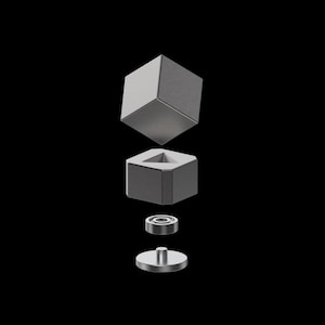 May include: A metallic grey cube-shaped object, shown disassembled. It features a square base with a triangular aperture. Components include a top cube, a base, a bearing, and a circular bottom piece. The background is solid black.