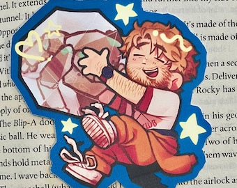 Op de afbeelding: Een sticker met een stripfiguur die een geometrische vorm omhelst. Het personage draagt een oranje broek, een wit shirt met "CLUB" en rode bretels. De sticker heeft een blauwe rand met gele sterren en een hart.