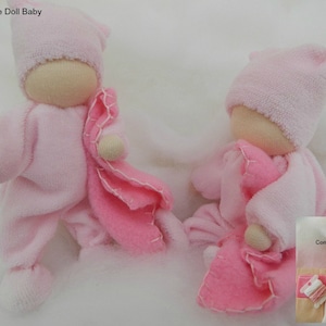 May include: Two handmade pink doll babies with matching hats and blankets. The dolls have beige fabric faces and limbs. The image includes a complete kit with materials to make the dolls. The text "Bendy Rope Doll Baby" is at the top of the image.