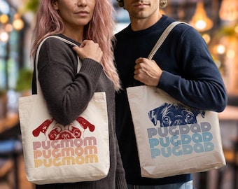 May include: Two off-white canvas tote bags. One bag features a red pug illustration with the text PUGMOM in a retro orange and yellow gradient font. The other bag features a dark blue pug illustration with the text PUGDAD in a blue gradient font.
