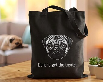 May include: A black tote bag featuring a white line-art illustration of a pug dog face centred on the front. Below the dog illustration, the text reads "Dont forget the treats." in a simple white sans-serif font. The bag has two black shoulder straps.