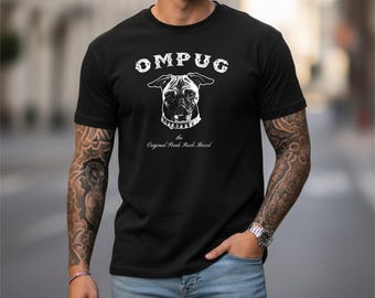 May include: A black short-sleeved t-shirt featuring a white graphic of a pug dog wearing a spiked collar. The text OMPUG is printed above the dog, and the text the Original Punk Rock Breed is printed below the dog in a white serif font.