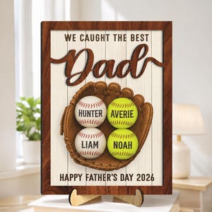 May include: Wooden sign with a brown frame and a white background. The sign reads "WE CAUGHT THE BEST Dad" in a script font. A baseball glove holds four baseballs, each with a name. The bottom reads "HAPPY FATHER'S DAY 2026".