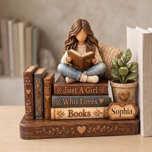 May include: A decorative figurine of a person with long brown hair sitting cross-legged on a stack of three books reading. The books are inscribed with the text Just A Girl Who Loves Books. A small potted plant and a nameplate reading Sophia are included.