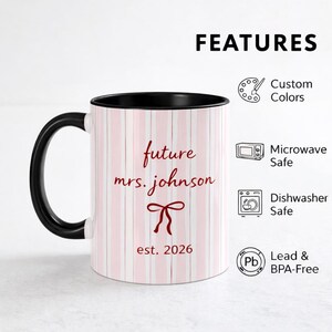 K&ouml;nnte beinhalten: Ein wei&szlig;er Becher mit schwarzem Griff und Rand, mit rosa vertikalen Streifen. Der Becher tr&auml;gt den Text "future mrs. johnson" in roter Schrift, zusammen mit einer Schleifengrafik und dem Jahr "est. 2026". Der Becher ist mikrowellen- und sp&uuml;lmaschinenfest.