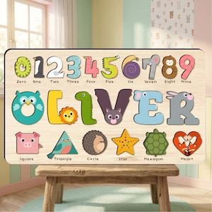 May include: Wooden educational puzzle featuring the name "OLIVER" and numbers 0-9. Each letter and number is a separate piece with animal and shape illustrations. The puzzle is designed for early learning and is displayed on a wooden stool.