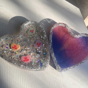 May include: Two heart-shaped resin trays. One is clear with glitter and candy hearts that say "BE MINE". The other is a gradient of pink and blue. These trays are perfect for Valentine's Day or as a decorative item.