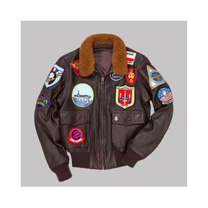 May include: A brown leather bomber jacket with a shearling collar and various embroidered patches. The jacket has a zip-up front, two front pockets, and ribbed cuffs and hem. Patches feature military and aviation-related designs.