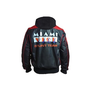 May include: Black leather jacket with a black hood and red accents. The back of the jacket features the words "MIAMI VICE STUNT TEAM" in white, orange, and blue lettering. The jacket has a ribbed hem and cuffs.
