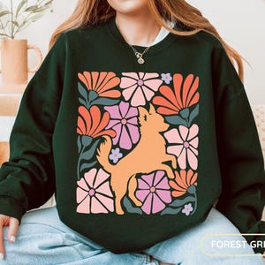 May include: Forest green sweatshirt featuring a retro floral design with an orange dog silhouette. The design includes orange, pink, and purple flowers. The sweatshirt is a solid forest green color.