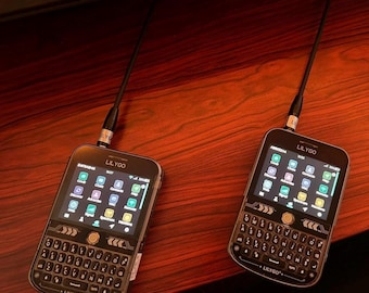 May include: Two black LILYGO handheld communication devices with QWERTY keyboards and colour touchscreens. Each device features a top-mounted antenna, a central navigation button, and a digital interface displaying various app icons and system status.