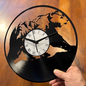 Może przedstawiać: Czarny zegar winylowy z sylwetką niedźwiedzia wspinającego się na górę. Tarcza zegara ma cyfry rzymskie i napis "KraftyVinyl".