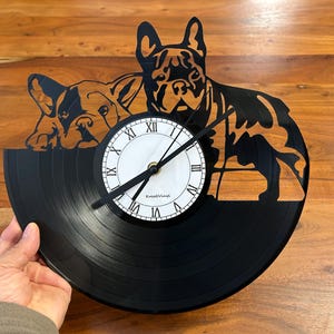Könnte beinhalten: Eine schwarze Schallplattenuhr mit weißem Zifferblatt und schwarzen Zeigern. Die Uhr ist mit einer Silhouette von zwei französischen Bulldoggen verziert.
