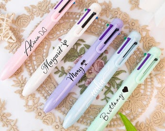 May include: Five multi-color pens in pastel shades of pink, white, lavender, light blue, and mint green. Each pen has a name written on it: Alicia, Margaret, Mary, Emilia, and Brittany. The pens are arranged on a decorative lace surface.