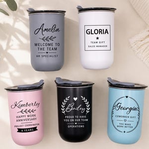 Puede incluir: Cinco vasos cilíndricos con tapa en gris, blanco, rosa, negro y azul claro. Cada uno presenta texto y gráficos negros personalizados, incluyendo nombres como Amelia, Gloria, Kimberly, Bailey y Georgia, junto con títulos profesionales.