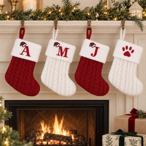 May include: Four Christmas stockings hanging in a row. Two are red with white cuffs and two are white with white cuffs. The stockings feature cable knit patterns. The cuffs are embroidered with the letters A, M, J, and a red paw print, each topped with a small Santa hat icon.