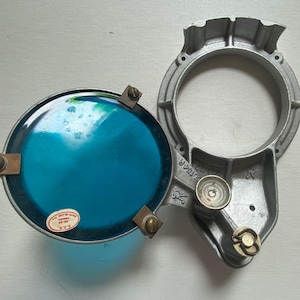May include: A vintage, silver-colored, metal light fixture with a blue glass lens. The fixture has a round opening and a small, round knob on the side. The lens has a small, round sticker with the text "MADE IN JAPAN" on it.