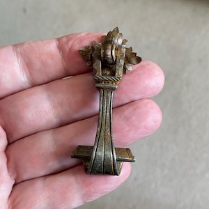 May include: A vintage, ornate, metal drawer pull with a decorative, scroll-like design. The pull is made of a silver-toned metal with a rustic finish.