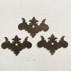 May include: Three antique brass decorative hardware pieces with a floral design. Each piece has a square hole in the center.