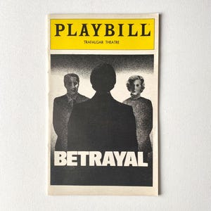 May include: Playbill for the play "Betrayal" at the Trafalgar Theatre. The cover features a yellow banner with the word "PLAYBILL" and the theater's name. Below, a black and white image depicts three figures.