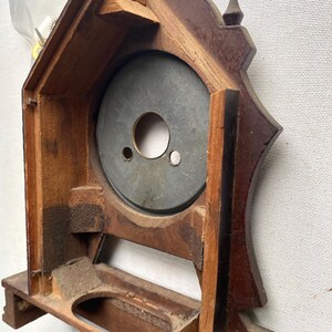 Puede incluir: Un marco de reloj de madera vintage con un acabado marr&oacute;n oscuro. El marco del reloj tiene una abertura circular para la esfera del reloj y una base rectangular. Los engranajes internos del reloj son visibles en la parte superior. El reloj es probablemente antiguo.