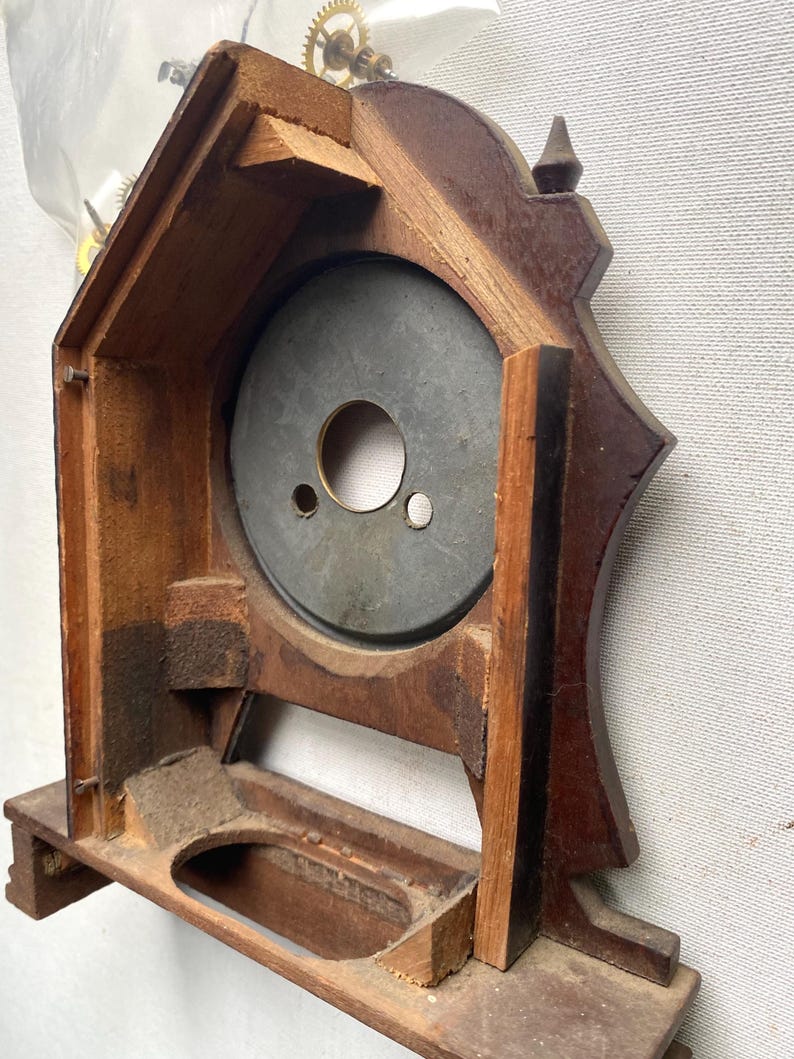 Puede incluir: Un marco de reloj de madera vintage con un acabado marr&oacute;n oscuro. El marco del reloj tiene una abertura circular para la esfera del reloj y una base rectangular. Los engranajes internos del reloj son visibles en la parte superior. El reloj es probablemente antiguo.