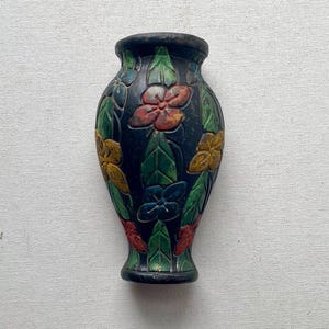 May include: A small, dark-colored vase with a floral design. The vase features colorful flowers in red, yellow, blue, and green, set against a dark background. The flowers are arranged in vertical patterns, adding a decorative touch to the vase.