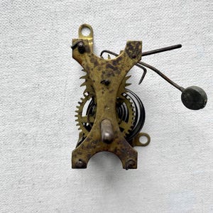 May include: A vintage clock movement with brass gears, springs, and a pendulum. The metal components show signs of age and wear, with a dark patina. The design includes a central support structure and various mechanical parts.