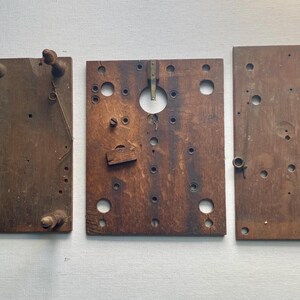 May include: Three weathered, rectangular wooden panels with various holes, pegs, and hardware. The panels are stained a dark brown color, showing signs of age and use. The panels appear to be components of a larger, possibly antique, item.
