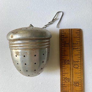 May include: Silver metal tea infuser shaped like an acorn with a chain and hook. The infuser is about 2 inches tall and has a diameter of about 1.5 inches.