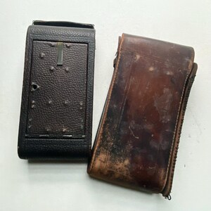 May include: Two rectangular cases. The left case is dark brown with a textured, pebbled surface and a small metal latch. The right case is a smooth, worn medium-brown leather with visible scuffs, scratches, and signs of age on its surface.