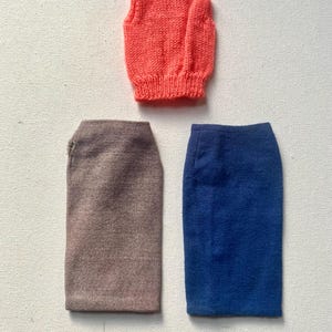 May include: An orange knitted vest with a high neck is displayed above two skirts. One skirt is a muted brown, and the other is a vibrant blue. The skirts are straight cut, and the vest is a solid color.