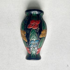 May include: A small, dark blue vase with a floral design. The flowers are red, yellow, and blue, with green leaves. The vase has a rounded body and a narrow neck, and is likely made of metal.